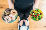 Eine Frau steht auf einer Waage und hält zwei Schüsseln mit Süssigkeiten und gesundem Salat  Eine Frau steht auf einer Waage und hält zwei Schüsseln mit Süssigkeiten und gesundem Salat